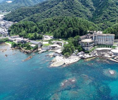 Aerial view of Hotel Kinparo on rocky coast with turquoise water and forested hills in Hyōgo, Kansai