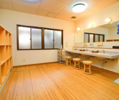 Communal changing room with wooden flooring, open shelving lockers, mirrored sinks and stools