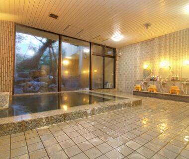 Large indoor soaking bath with tiled floor, shower stools and garden-facing window at Hotel Kinu, Tochigi