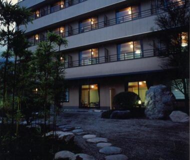 Stone path leads through garden to lit entrance and balconies at Hotel Kinu in Tochigi