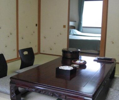 Traditional tatami room with low wooden table, zabuton cushions and sliding fusuma doors opening to a room with a bed