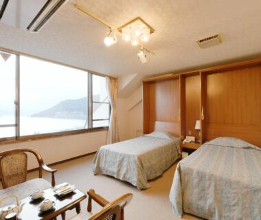 Western twin room with large window overlooking lake and mountains, seating area and bedside table