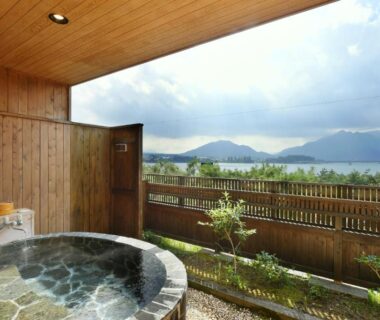 Outdoor stone bath on wooden terrace overlooking lake and mountains at Hotel Koryu, Yamanashi