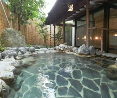 Stone-lined outdoor onsen with wooden veranda and bamboo fence at Hotel Koryu, Yamanashi
