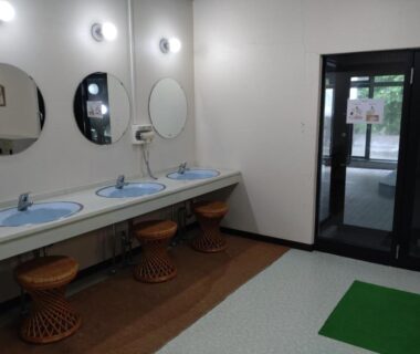 Three washbasins with round mirrors, wicker stools and doorway leading to bathing area at Hotel Kosho in Tochigi