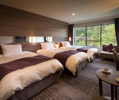 Three single beds in a modern ryokan room with window view of trees and small seating area