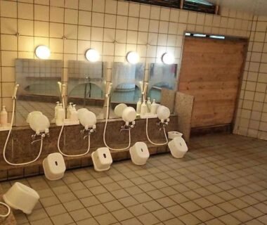Tiled communal bathing wash stations with stools, handheld showers and mirrors at Hotel Manyotei in Tochigi