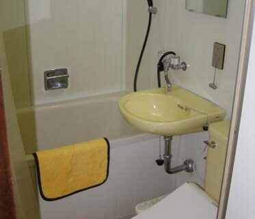 Compact unit bath with tub, handheld shower, small yellow sink and towel at Hotel Masyu, Hokkaidō