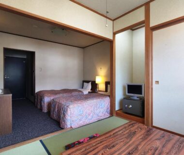 Room combining tatami area and twin beds with low table, bedside lamp and compact TV at Hotel Meribel Tsugaike Nagano