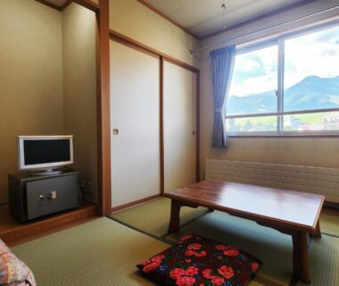 Tatami room with low wooden table, floral cushion, sliding doors, television on stand and mountain view