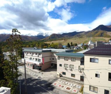 Low-rise ryokan buildings and parking lot with surrounding mountains at Hotel Meribel Tsugaike in Nagano, Chūbu Japan