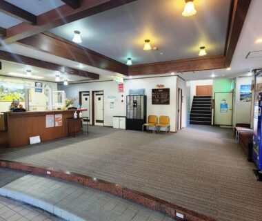 Spacious ryokan reception area with front desk, seating, vending machine and staircase at Hotel Meribel Tsugaike in Nagano