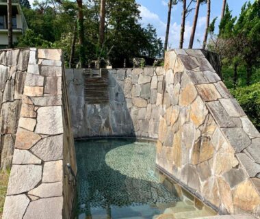 Outdoor stone bath with clear water and surrounding pine trees at Hotel Miki in Gifu