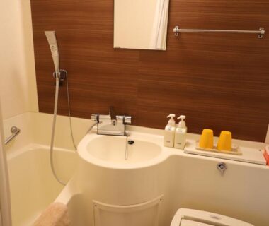 Compact bath unit with tub, handheld shower, sink, mirror and toiletries at Hotel Mimatsu in Nara