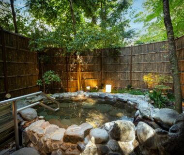 Stone onsen bath framed by bamboo fence and greenery at Hotel Nanpuso in Kanagawa