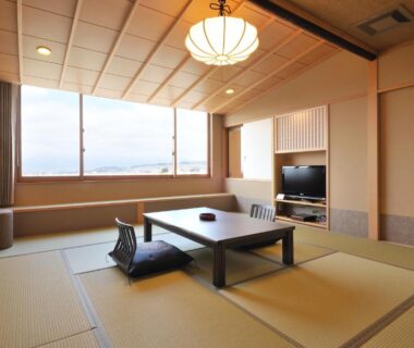 Tatami room with low table, floor chairs, TV and large window at Hotel New Kotobuki in Nagano