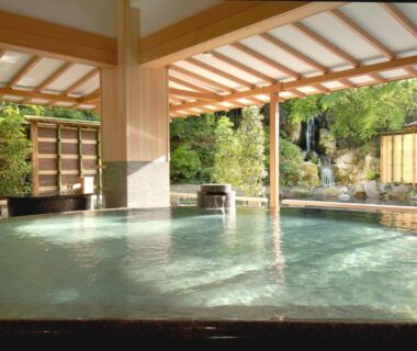 Indoor onsen bath with wooden beams and tranquil garden view at Hotel New Mitoya, Miyagi