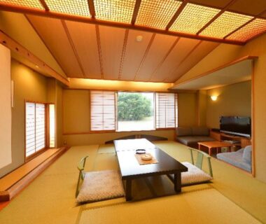 Spacious tatami room with low table, zabuton cushions, shoji screens and greenery view at Hotel New Mitoya in Miyagi