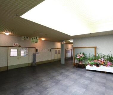 Spacious tiled lobby with large ceiling light panel and floral bench by entrance doors