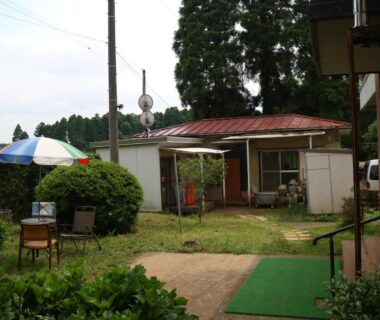 Outdoor courtyard with umbrella-shaded table, chairs, lawn and small single-story building at Hotel New Otani in Chiba