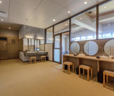 Dressing area with round mirrors, wooden stools, lockers and sinks at Hotel New Tsuruta, Ōita