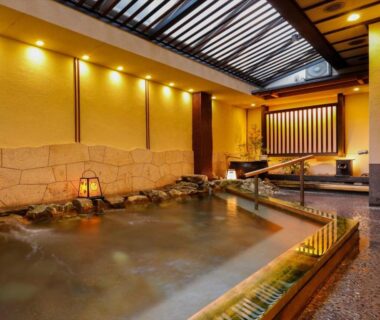 Warm indoor onsen with stone edging, wooden railings and skylight at Hotel New Wakasa in Nara