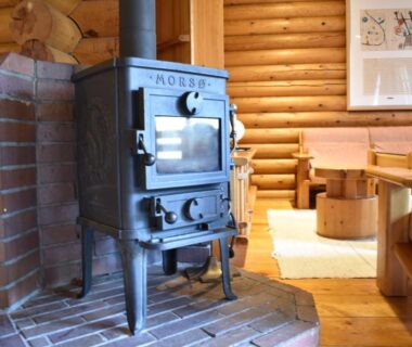Cast iron wood stove on brick hearth inside a log cabin style ryokan lounge with wooden seating