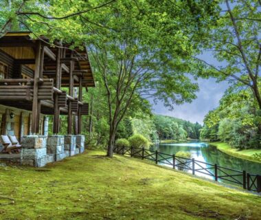 Wooden lodge exterior beside tranquil pond with tree-lined grassy lawn at Hotel Nidom in Hokkaidō