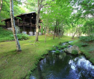 Clear woodland stream with mossy banks and a wooden lodge of Hotel Nidom in Hokkaido forest setting