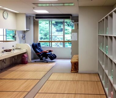 Tatami relaxation area with sinks, massage chair and lockers overlooking greenery at Hotel Nosegawa Nara