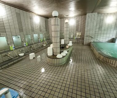 Tiled communal bathing area with shower stations, stools, mirrors and a soaking pool at Hotel Nosegawa in Nara