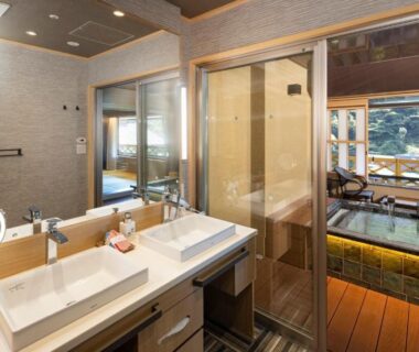 Double sink vanity leading to wooden bathing area and sliding glass partition with garden view at Hotel Okada Kanagawa