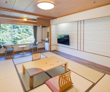 Tatami room with low table, floor cushions, shoji panels and window overlooking green hillside at Hotel Okada Kanagawa