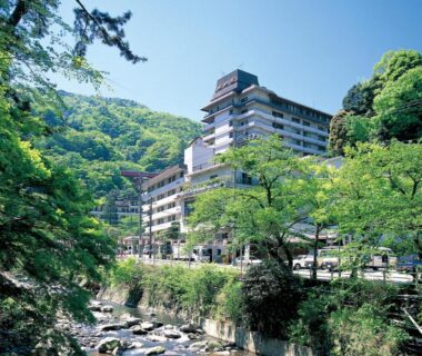 Riverside multi story ryokan building beside a rocky stream surrounded by verdant hills in Kanagawa