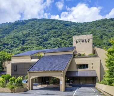 Entrance and facade of Hotel Okuyumoto with green mountain backdrop in Kanagawa, Kanto