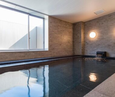 Tiled indoor communal bath with large window and stone edging at Hotel Ole, Shizuoka