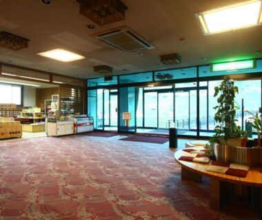 Carpeted ryokan lobby with seating, souvenir displays and glass entrance at Hotel Omodaka Nagano
