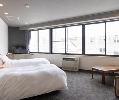 Bright twin room with two white beds, low wooden table, armchair and large windows at Hotel & Onsen 2307 Shigakogen