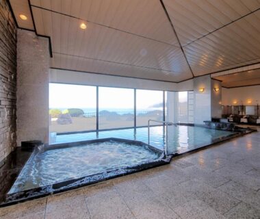 Indoor onsen pools with floor-to-ceiling windows and stone edging overlooking distant horizon