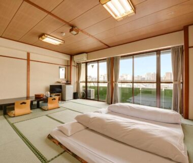 Traditional tatami room with futon bedding, low table and large windows overlooking Kyoto cityscape at Hotel Oumiya