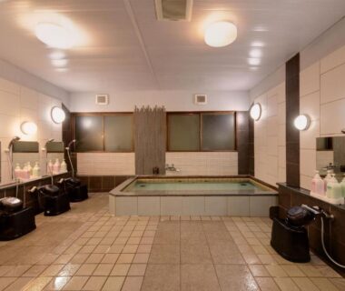 Tiled communal bathing area with stools, wall-mounted showers and central soaking tub at Hotel Oumiya, Kyoto