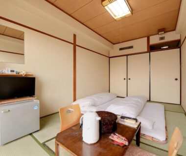 Traditional tatami room with futon bedding, low wooden table, kettle, TV and compact refrigerator at Hotel Oumiya Kyoto