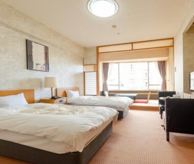 Western-style beds, bedside lamps, carpeted floor, seating alcove by window with sliding screens and low table