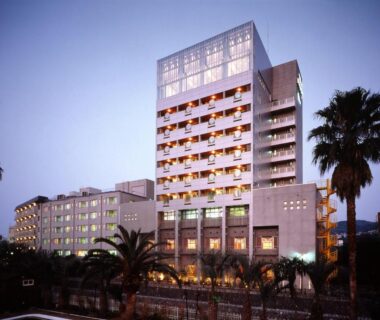 Dusk view of multi-story Hotel Ravie Kawaryo with palm trees in Shizuoka, Chūbu region