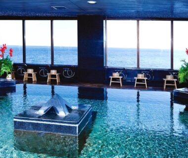 Spacious indoor onsen pool with low stools and ocean view at Hotel Resorpia Atami, Shizuoka