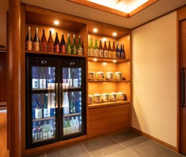Refrigerated display case and wooden shelves stocked with sake bottles in Hotel Saginoyu corridor, Nagano