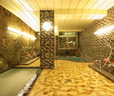 Communal indoor onsen with stone walls, shower stations, and tiled soaking pool at Hotel Sanraku in Nagano