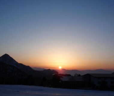 Sun rising behind mountain ridge with snowy foreground and low buildings in Nagano, Chūbu