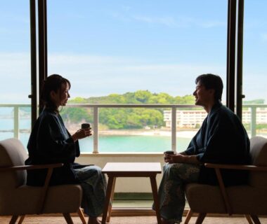 Two guests in yukata seated by window with bay and small island view at Hotel Sanrakuso, Wakayama
