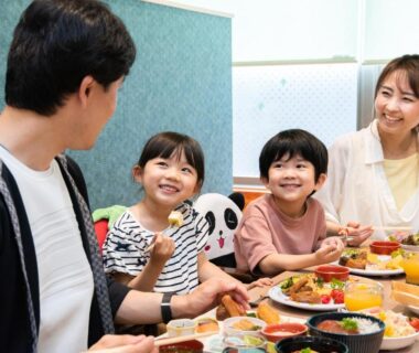 Family smiling around a breakfast table with traditional Japanese dishes in ryokan dining room, Hotel Sanrakuso, Wakayama